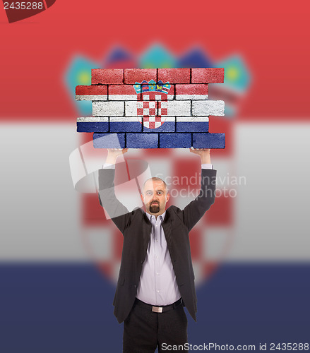 Image of Businessman holding a large piece of a brick wall