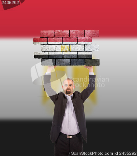 Image of Businessman holding a large piece of a brick wall