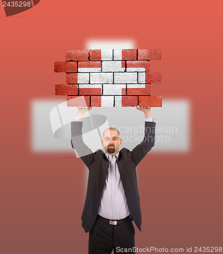 Image of Businessman holding a large piece of a brick wall