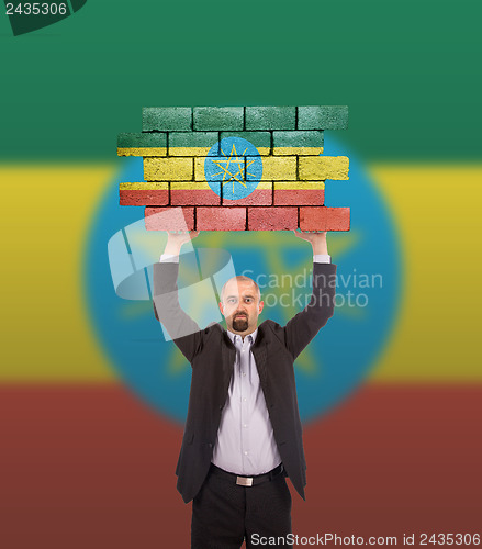 Image of Businessman holding a large piece of a brick wall