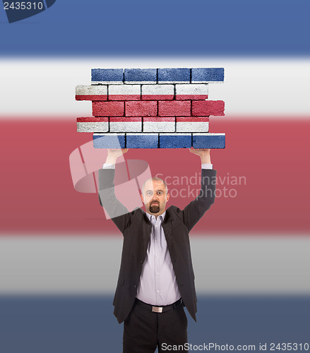 Image of Businessman holding a large piece of a brick wall