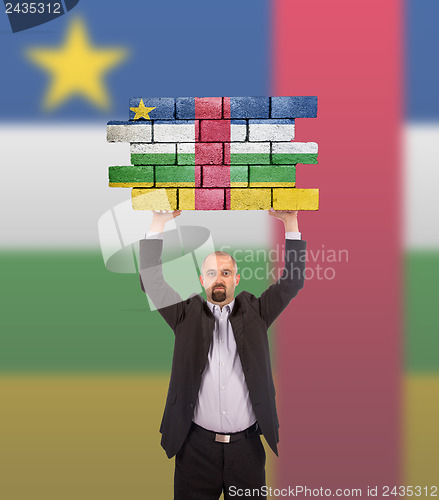 Image of Businessman holding a large piece of a brick wall