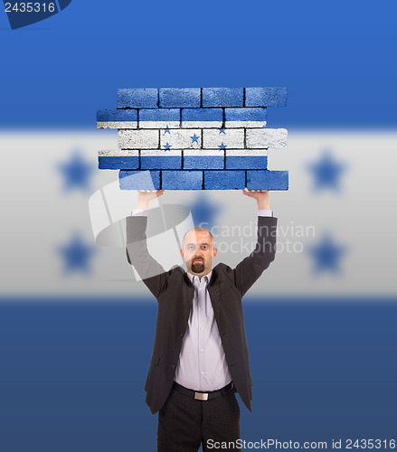 Image of Businessman holding a large piece of a brick wall