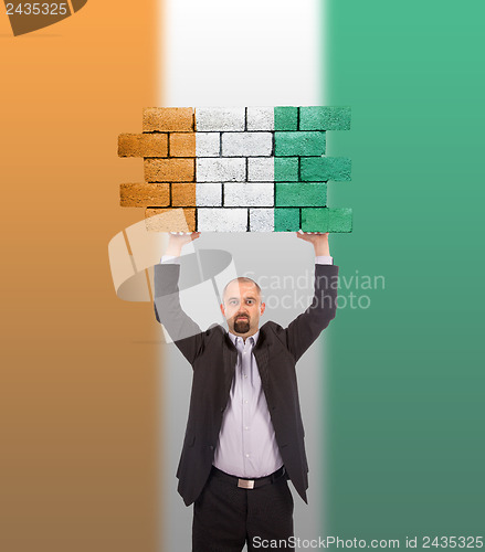Image of Businessman holding a large piece of a brick wall