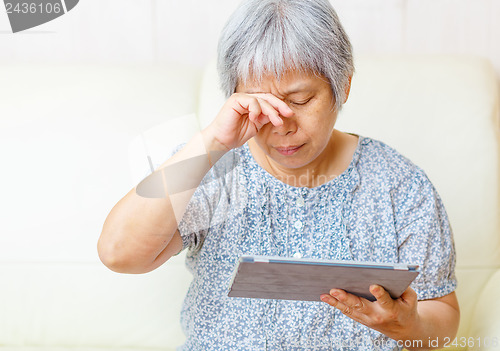 Image of Asian old woman using digital tablet with tired eyes