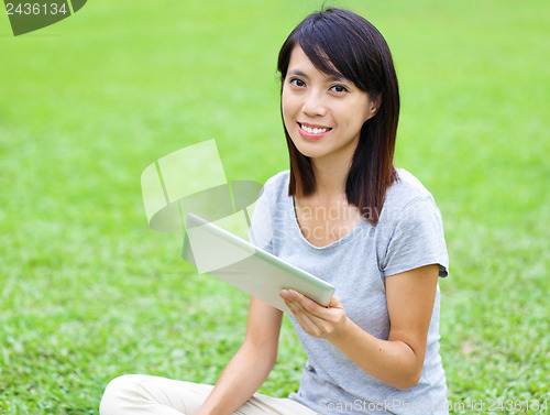 Image of Asian woman setting on grass with tablet