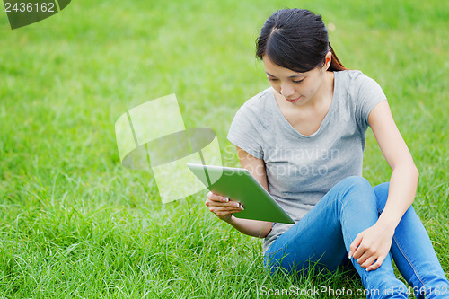 Image of Woman sitting on grass with tablet computer