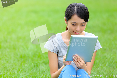 Image of Woman setting on grass with tablet 