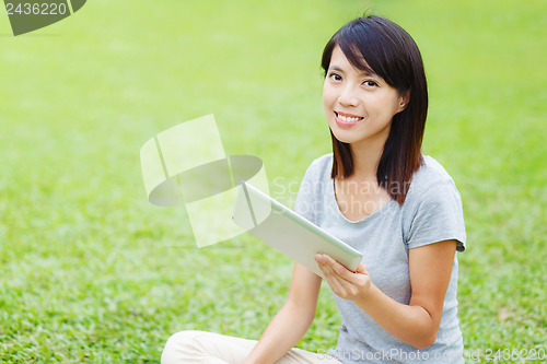 Image of Asian woman sitting on the lawn with tablet