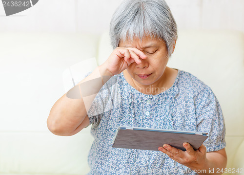 Image of Asian old woman using digital tablet with tired eyes