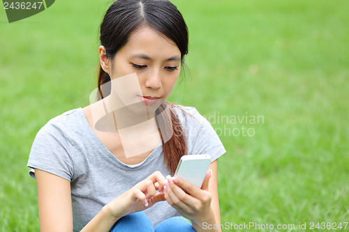 Image of Asian woman using smartphone on grass