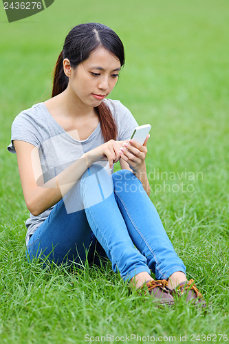 Image of Woman sitting on grass with smartphone