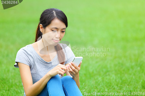 Image of Woman sitting on grass with smartphone