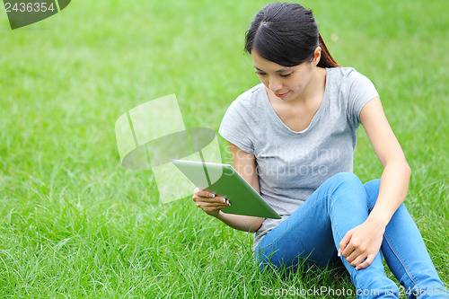 Image of Woman sitting on grass with tablet computer