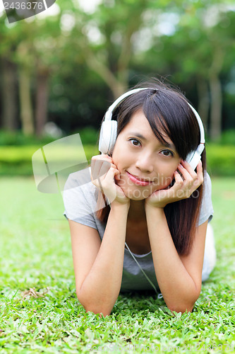 Image of Asian woman listen to song lying on grass