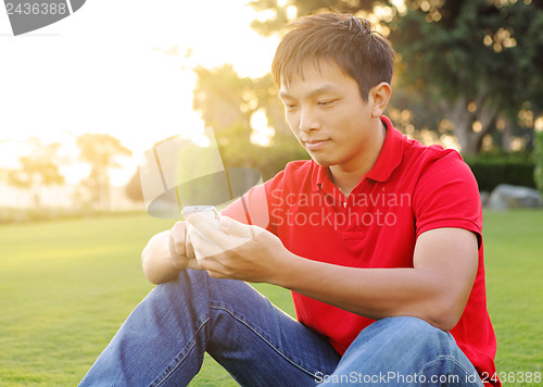 Image of man sits on grass and use mobile phone