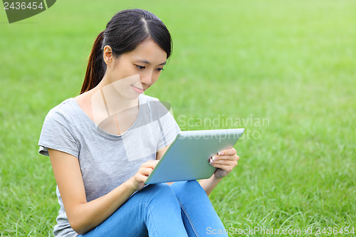 Image of Woman sitting on grass with tablet computer