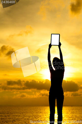 Image of Silhouette of woman holding tablet computer at sunset