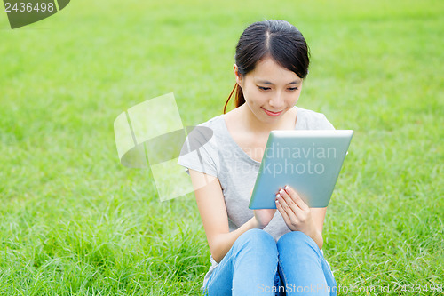 Image of Woman sitting on grass with tablet computer