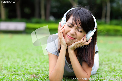 Image of Asian woman listen to song lying on grass