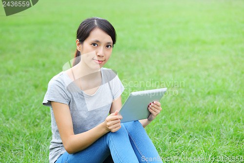 Image of Woman sitting on grass with tablet computer