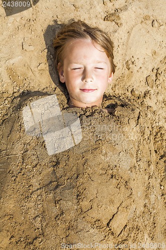 Image of happy boy dig oneself in the sand