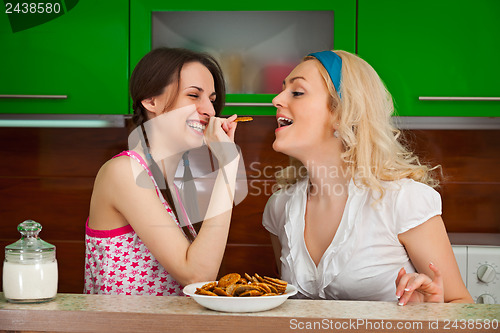 Image of Two young girls funny testing the cookies in the kitchen