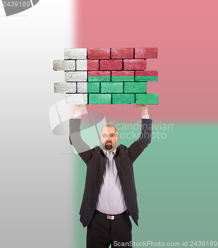 Image of Businessman holding a large piece of a brick wall