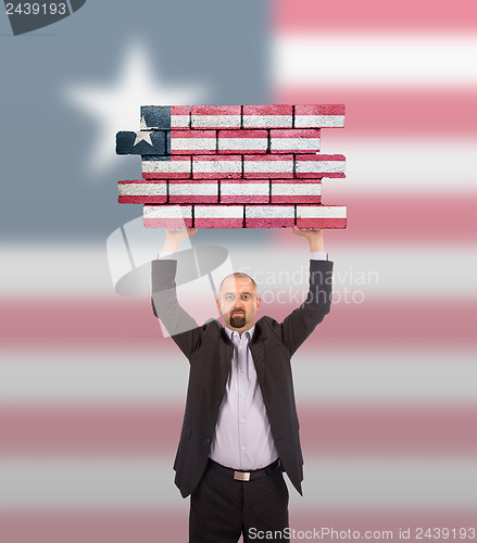 Image of Businessman holding a large piece of a brick wall