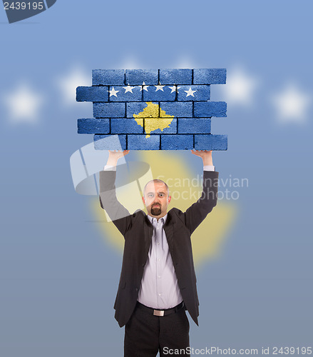 Image of Businessman holding a large piece of a brick wall