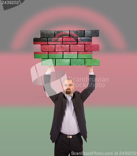 Image of Businessman holding a large piece of a brick wall