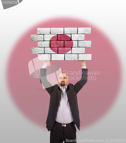 Image of Businessman holding a large piece of a brick wall