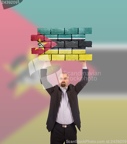 Image of Businessman holding a large piece of a brick wall