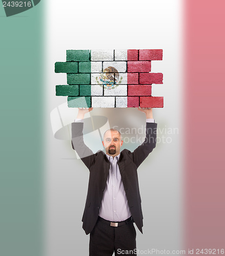 Image of Businessman holding a large piece of a brick wall