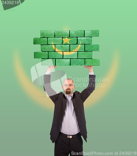 Image of Businessman holding a large piece of a brick wall