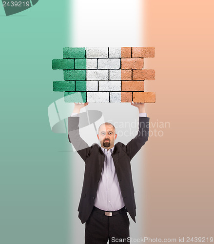 Image of Businessman holding a large piece of a brick wall