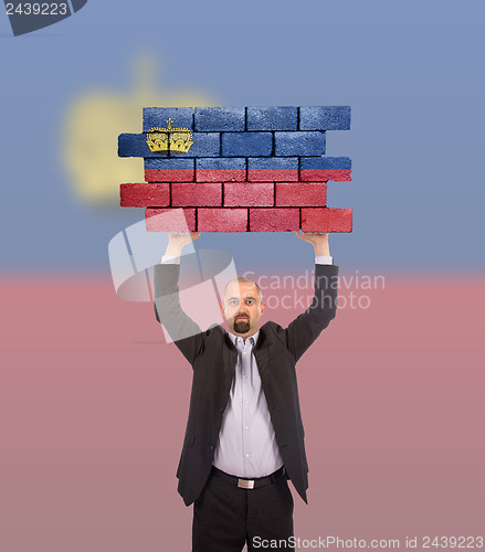 Image of Businessman holding a large piece of a brick wall