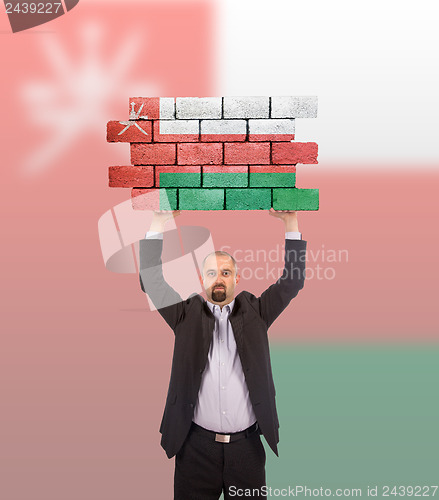 Image of Businessman holding a large piece of a brick wall