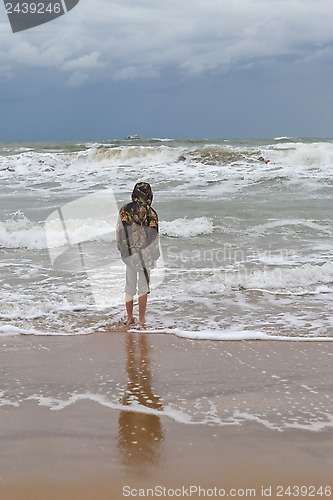 Image of The teenager costs on the seashore in a jacket and barefoot. 