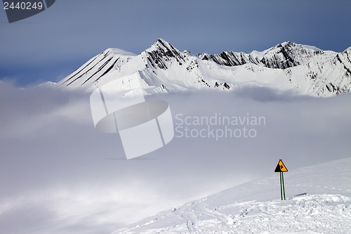 Image of Warning sing on ski slope and mountains in fog