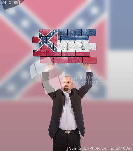 Image of Businessman holding a large piece of a brick wall