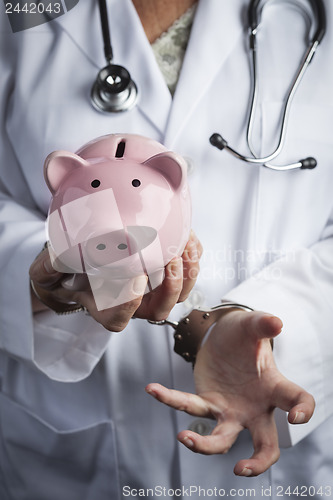Image of Doctor In Handcuffs Holding Piggy Bank Wearing Lab Coat, Stethos