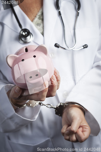 Image of Doctor In Handcuffs Holding Piggy Bank Wearing Lab Coat, Stethos