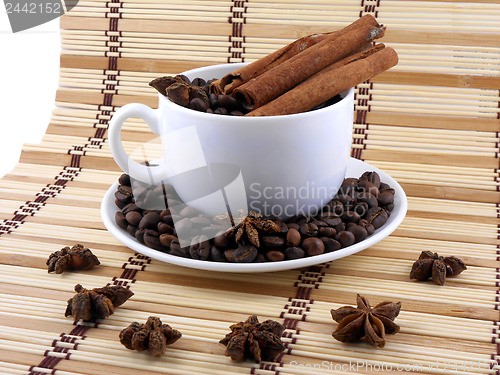 Image of white cup with coffee and cinnamon near star anise over bamboo table