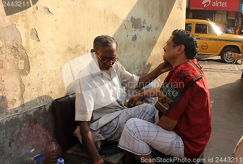 Image of Street barber shaving a man on a street in Kolkata