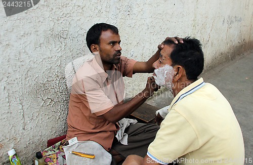 Image of Street barber shaving a man on a street in Kolkata