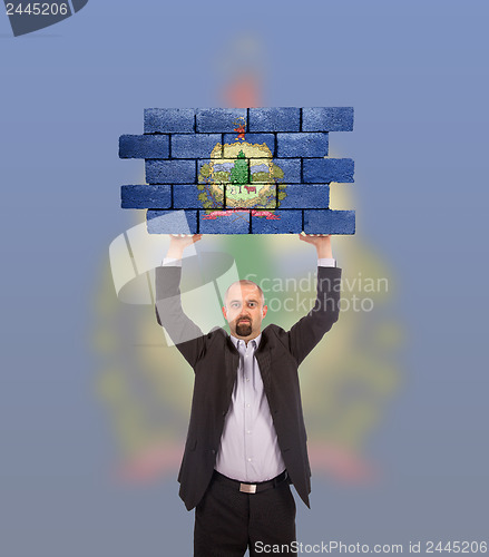 Image of Businessman holding a large piece of a brick wall