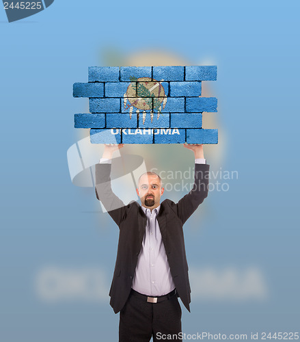 Image of Businessman holding a large piece of a brick wall