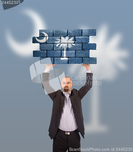 Image of Businessman holding a large piece of a brick wall