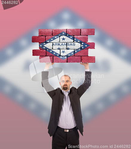 Image of Businessman holding a large piece of a brick wall